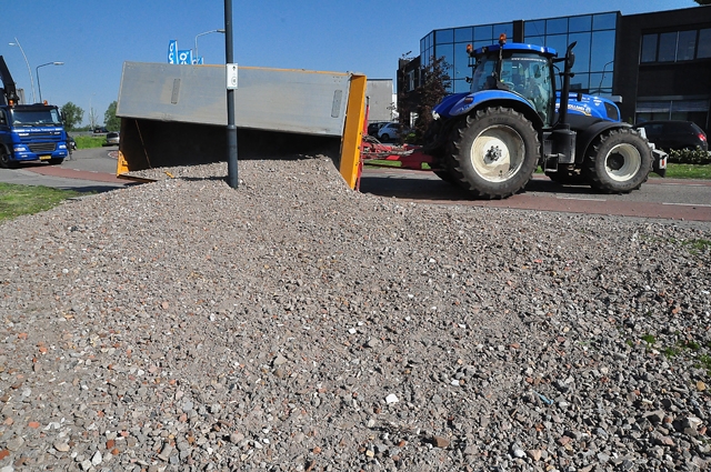 Tractor met aanhanger maakt uitwijkmanoeuvre in bocht, aanhanger met stenen slaat om
